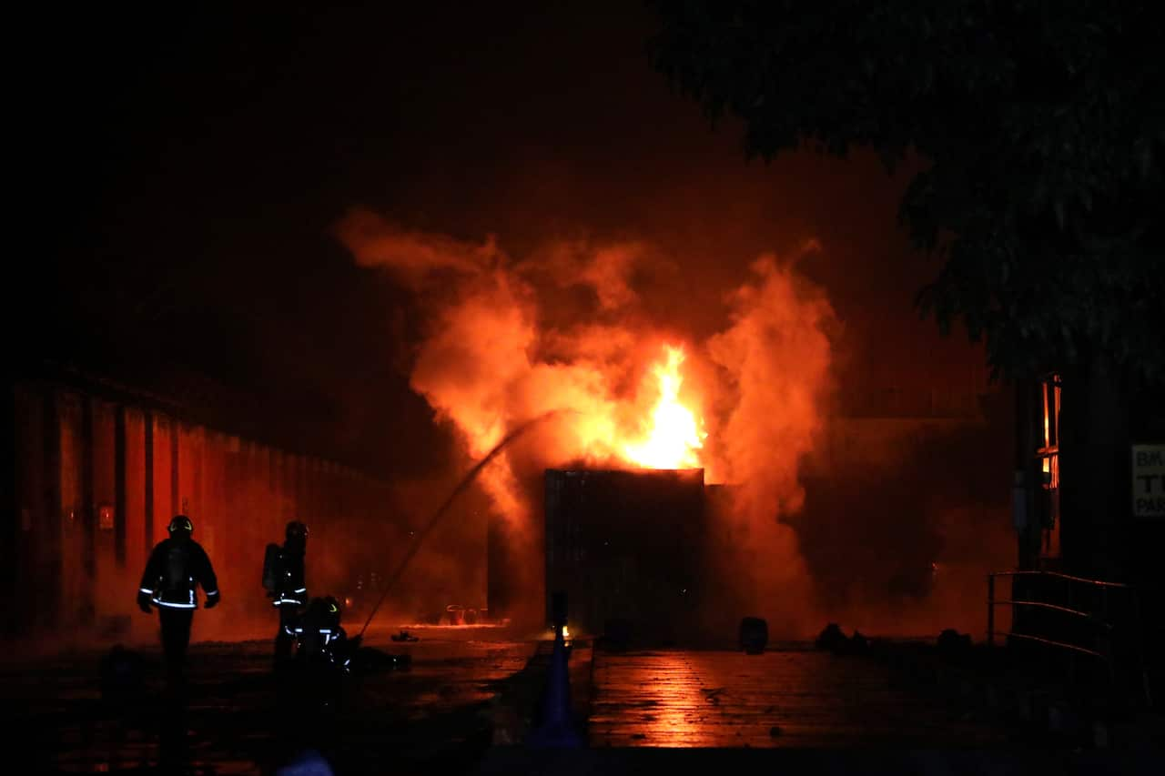 An overwhelming fire is being contained by two firefighters with a gust of water. 