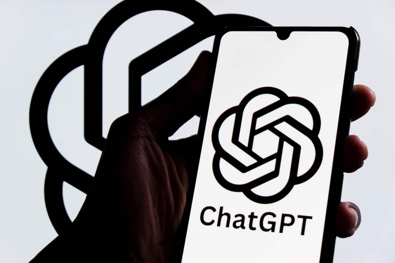 A hand holding a phone in front of a screen showing the OpenAI logo