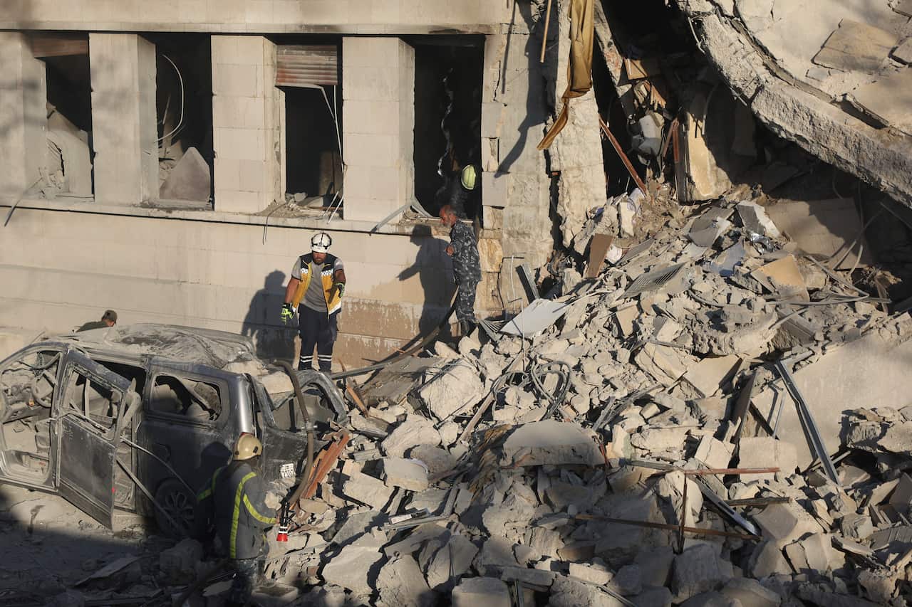 People standing amid a large pile of rubble from a damaged building.
