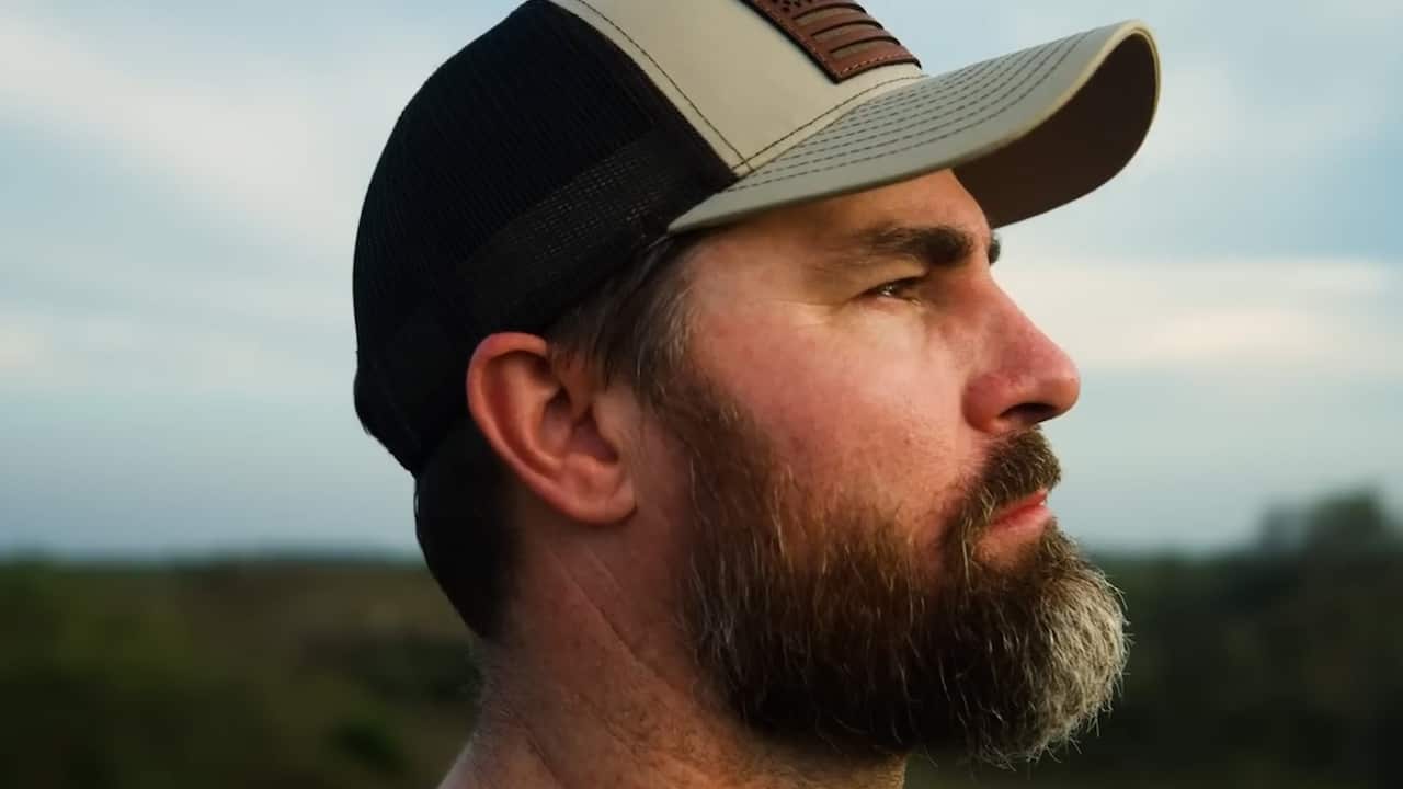 Side close-up view of a man with a beard wearing a cap