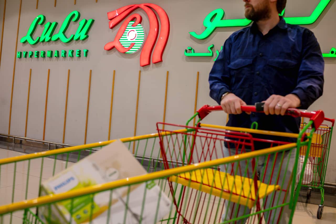 A man in a blue shirt is pushing a trolley with a Lulu Supermarket sign in the background.