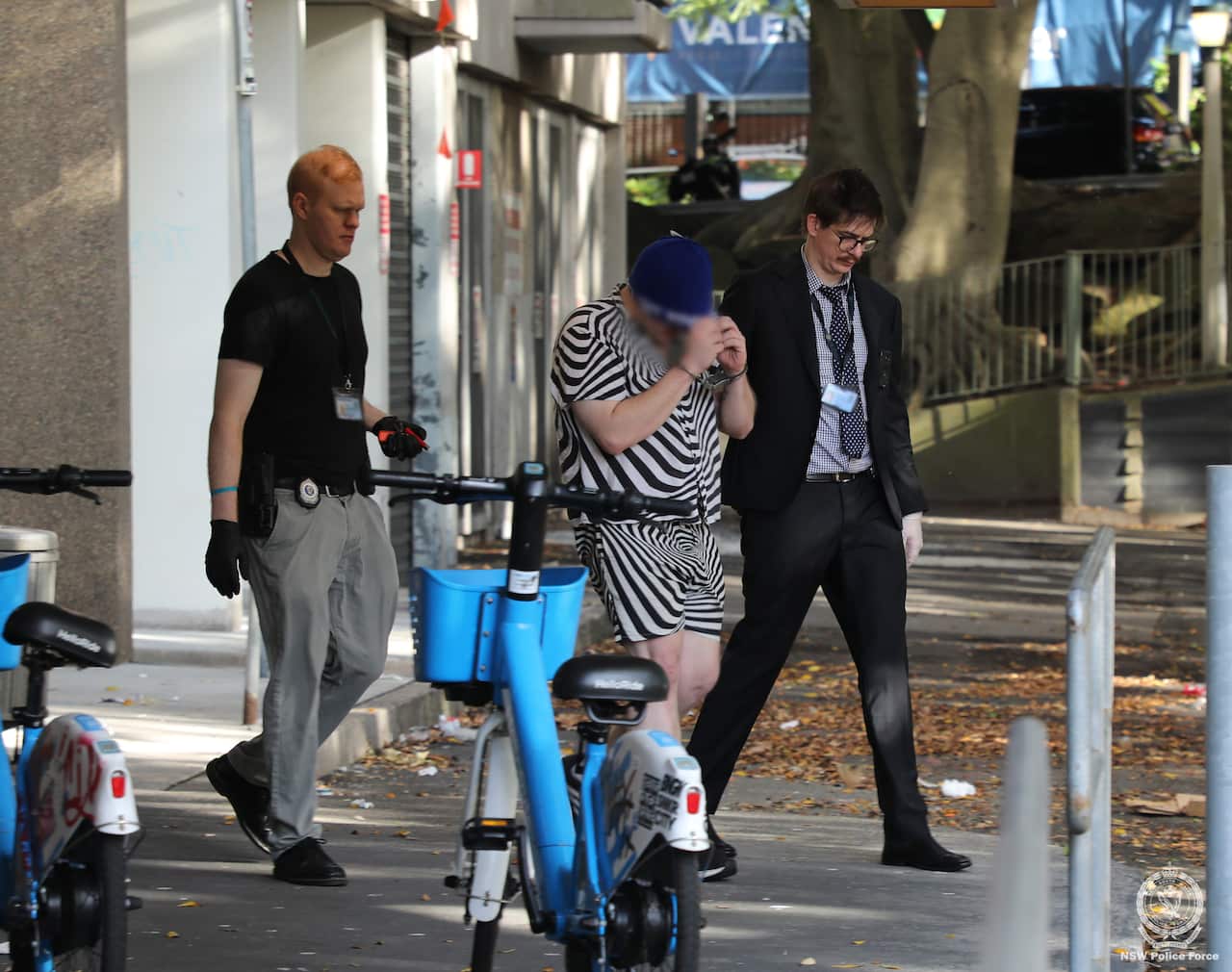Two plain-clothes policemen walk with a man wearing 