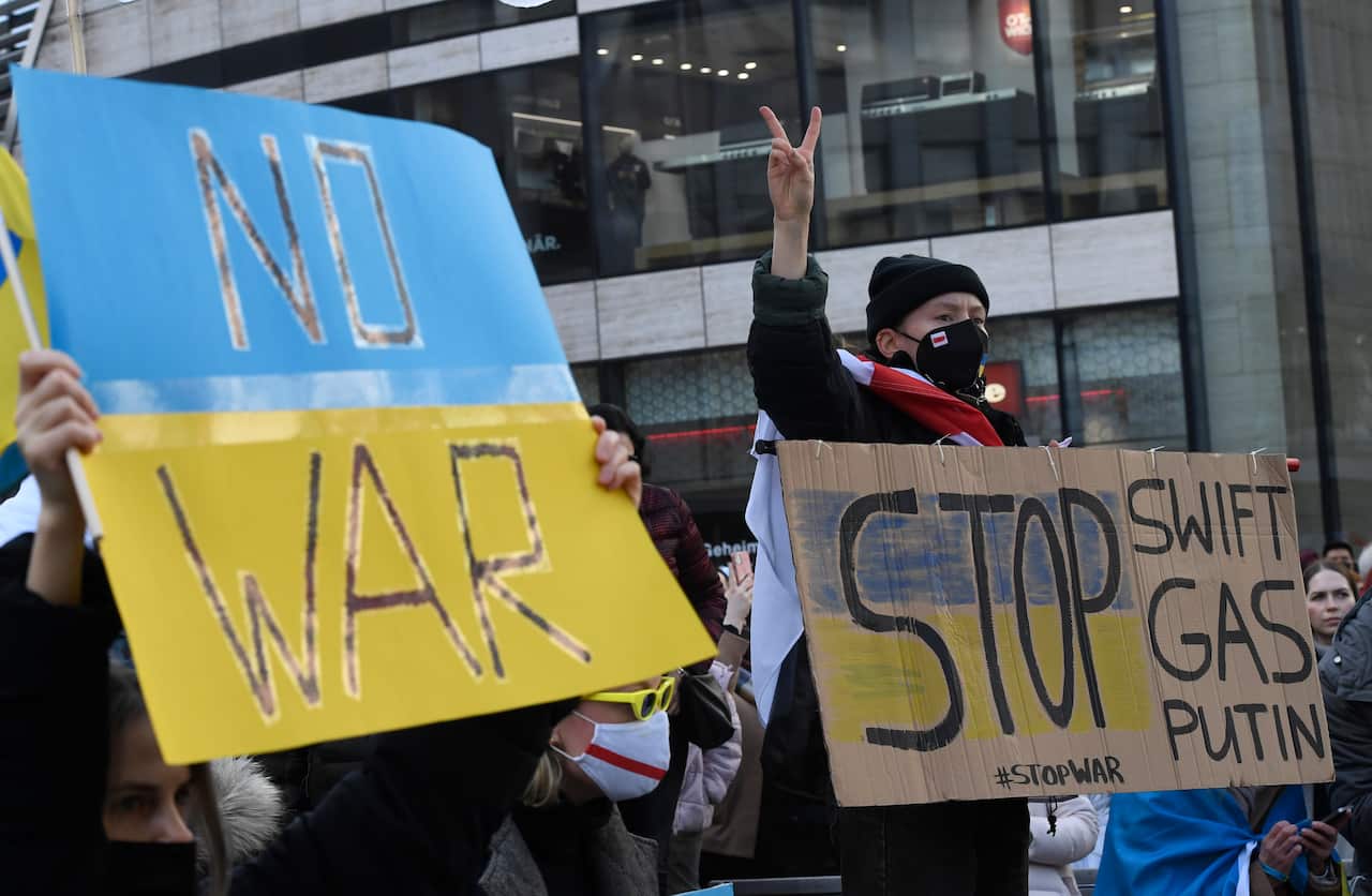 People hold signs reading "No War" and "Stop Swift, Gas, Putin", painted blue and yellow. 