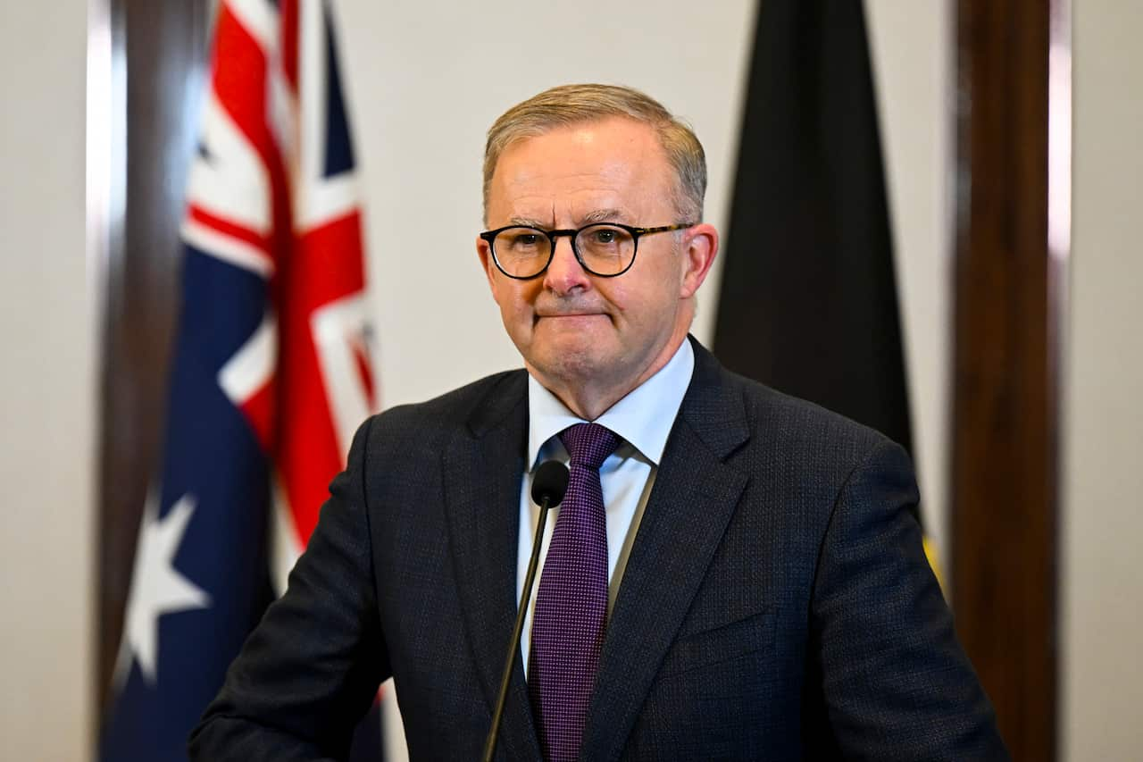 Albanese stands at a podium, press-lipped, in a suit