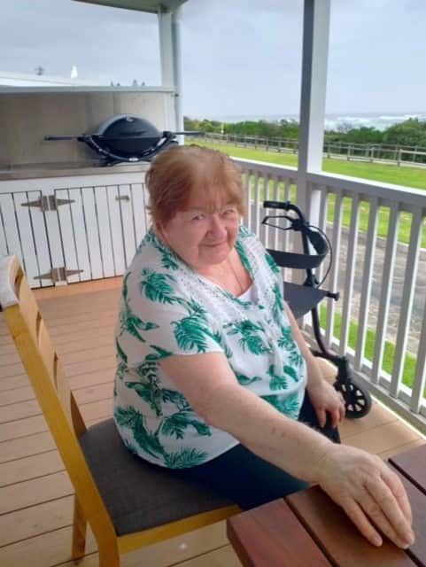 A woman is pictured sitting on a deck, smiling.