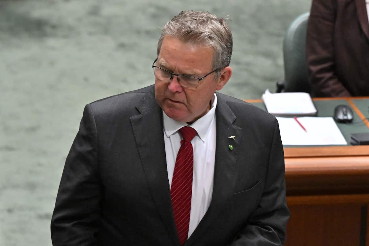 A grey haired men with glasses, looking to the side.