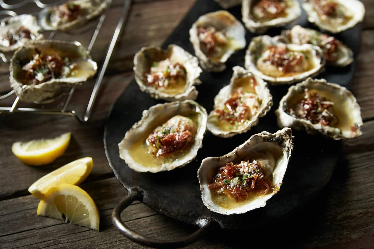 Juicy oysters sit on a round black metal tray, with slices of lemon alongside.
