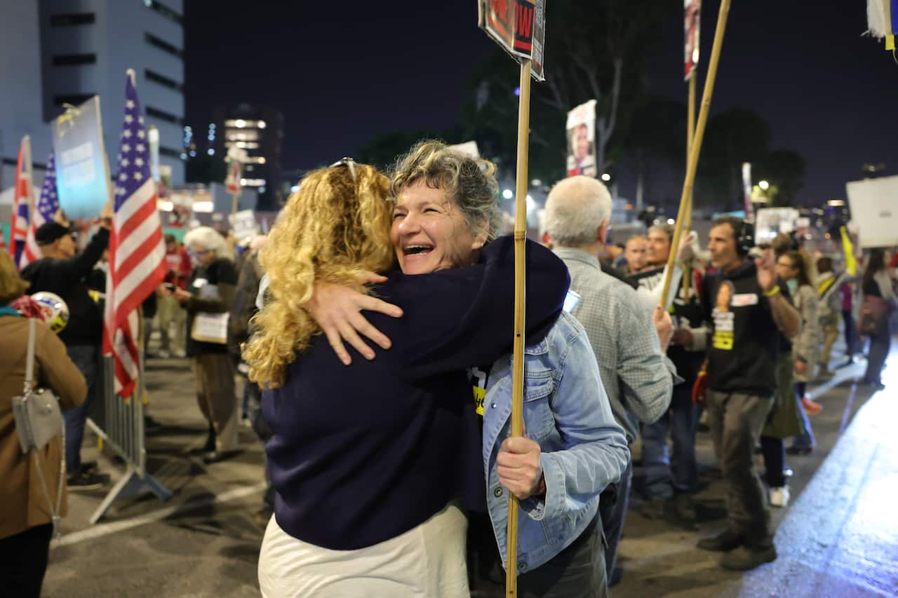 Two women embrace each other as people celebrate in the background.