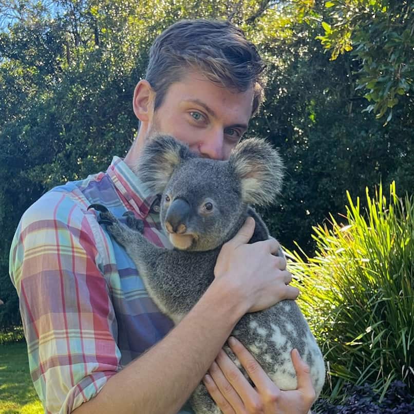 Man in a checkered shirt holding a koala outside