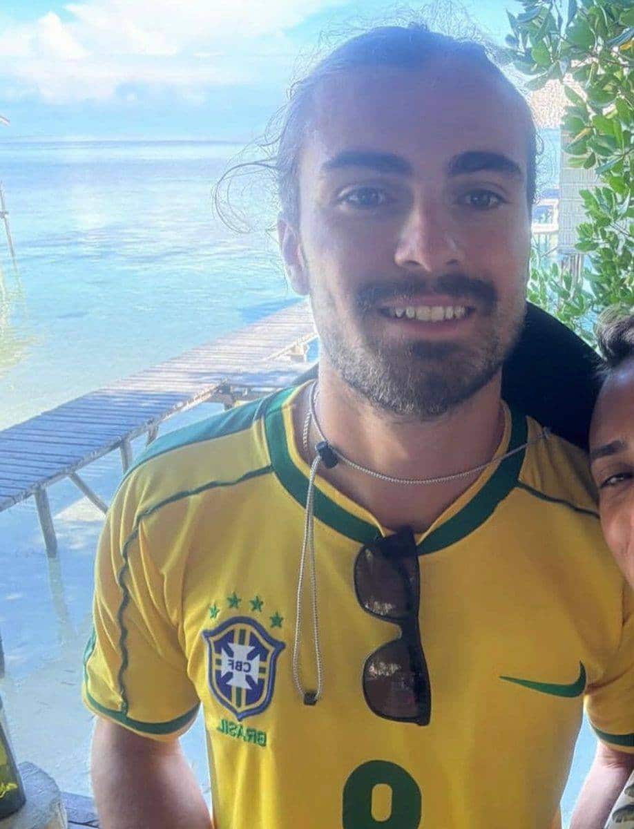 A man dressed in a yellow Brazil football jersey smiles into the camera. 