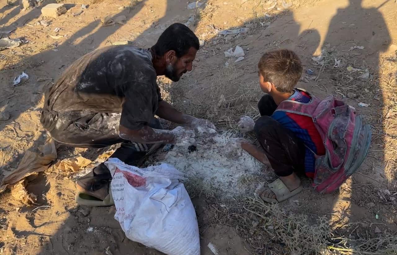 Man and child kneel to pick flour out of dirt