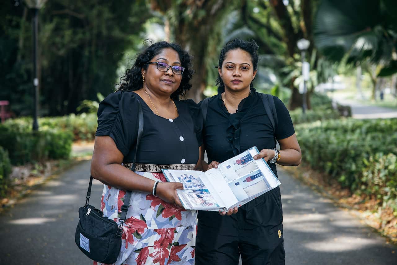 'Antrian' eksekusi: Bagaimana sikap keras Singapura terhadap kejahatan mengakibatkan kematian Pannir 1 Dua wanita berdiri di jalan setapak di taman, membuka album foto. Mereka berdua memiliki ekspresi wajah yang netral