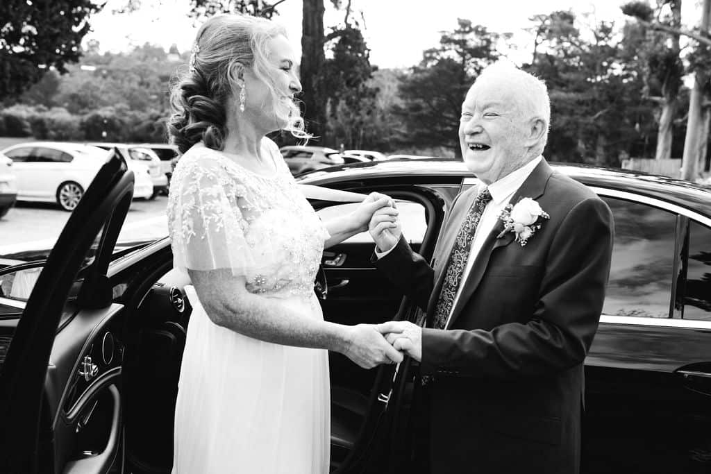 Megan in her wedding dress holds hands with her father on her wedding day.