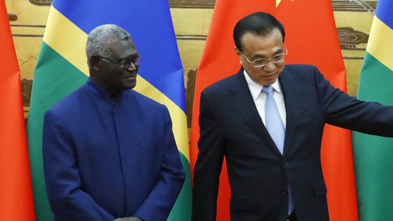 Two men standing in front of flags of China and Solomon Islands.