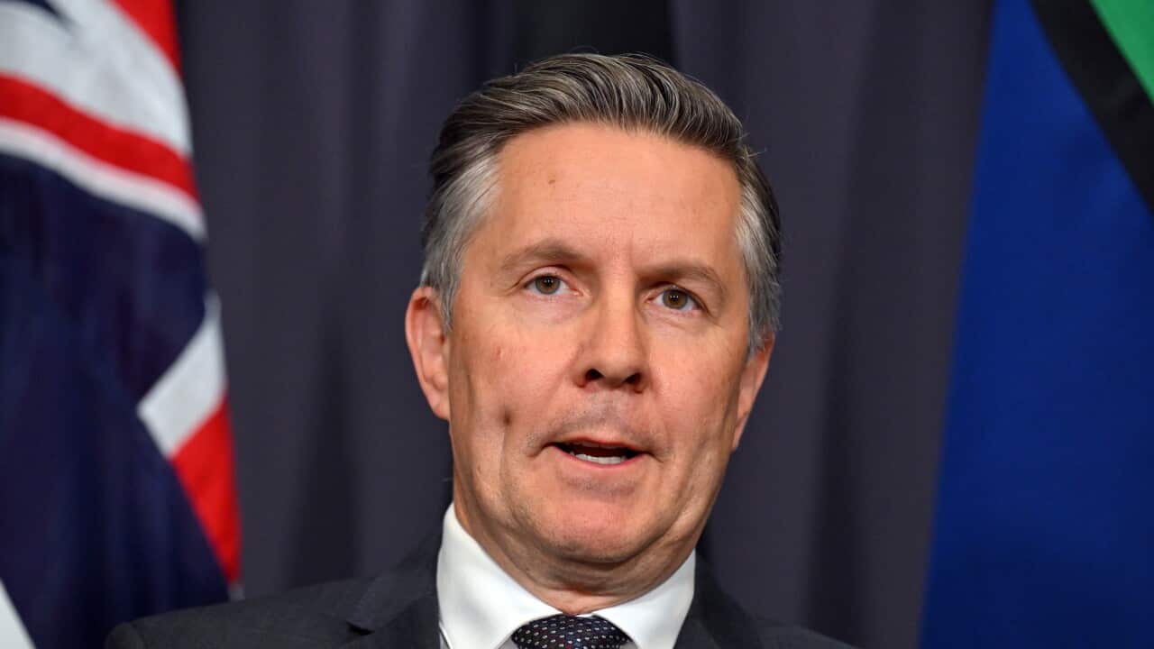 Man in a suit speaking at a podium with Australian flags behind him.