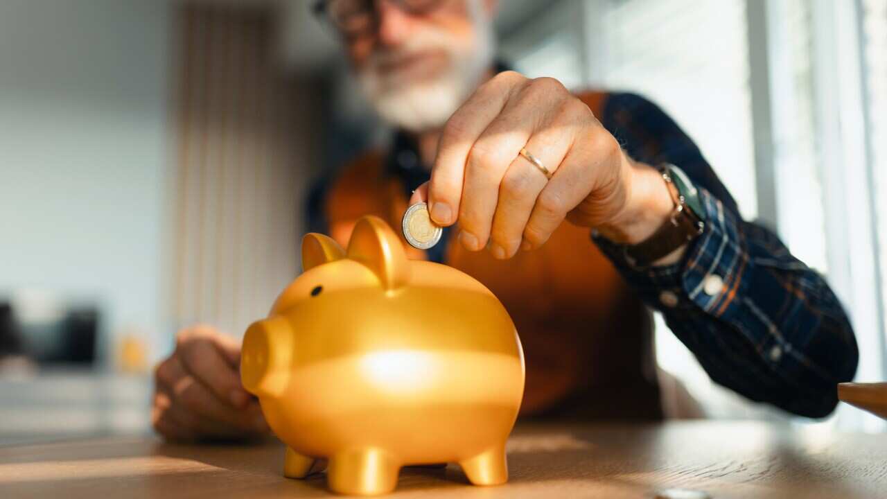 Senior man putting coins, money into a piggy bank. Saving Money after retirement, preparing for retirement. Financial education and financial literacy for seniors.