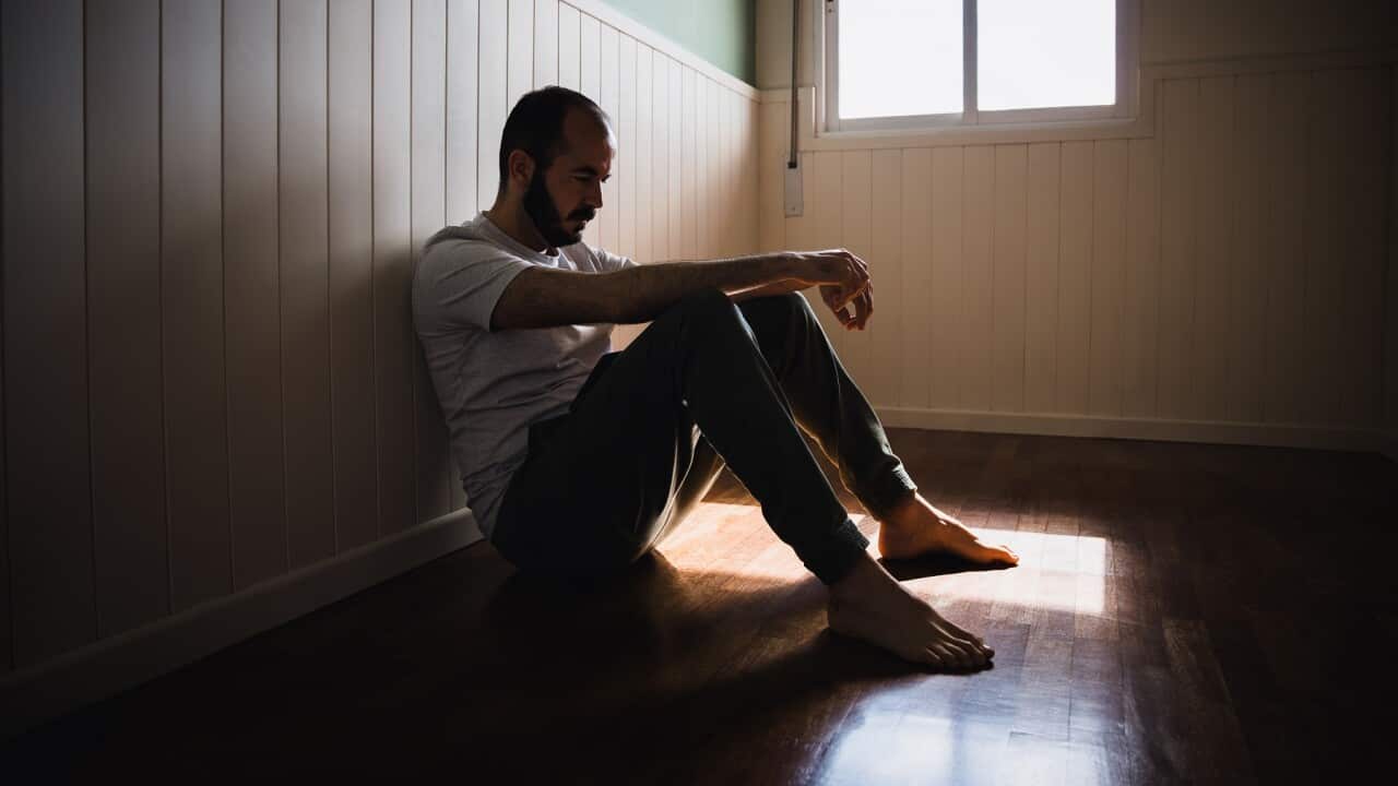 Lonely man sitting on floor by wall in dark room feeling sad