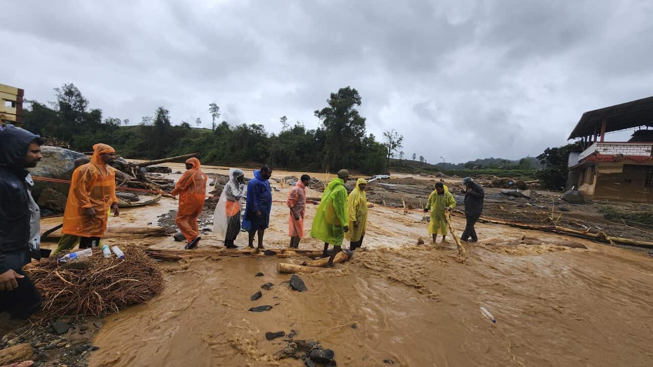 A group of people in raincoats cross a muddy river
