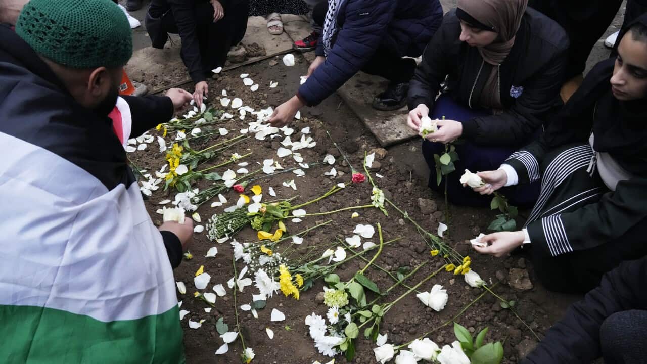A man draped in the Palestinian flag and several women wearing hijabs drape flowers on a grave