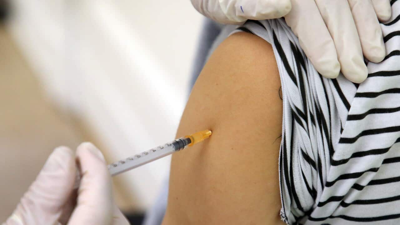 A gloved hand inserts a needle into a person's arm