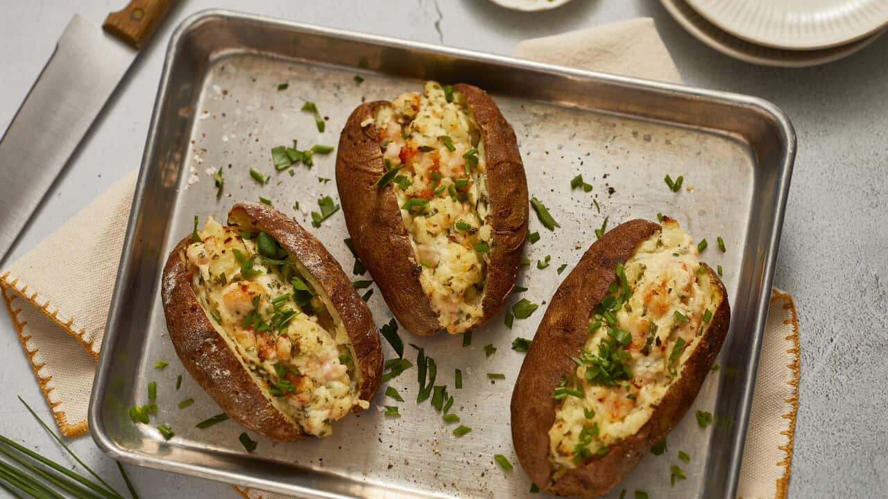 Three baked potatos with a potato and prawn filling sit on a metal baking tray. The potato is scattered with fresh chopped herbs.