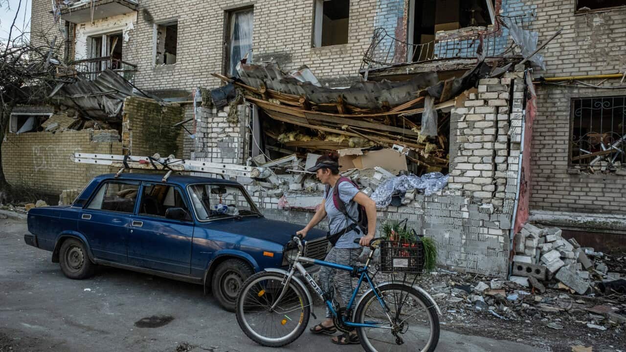 A woman with her bike in the Donbas in front of a destroyed building