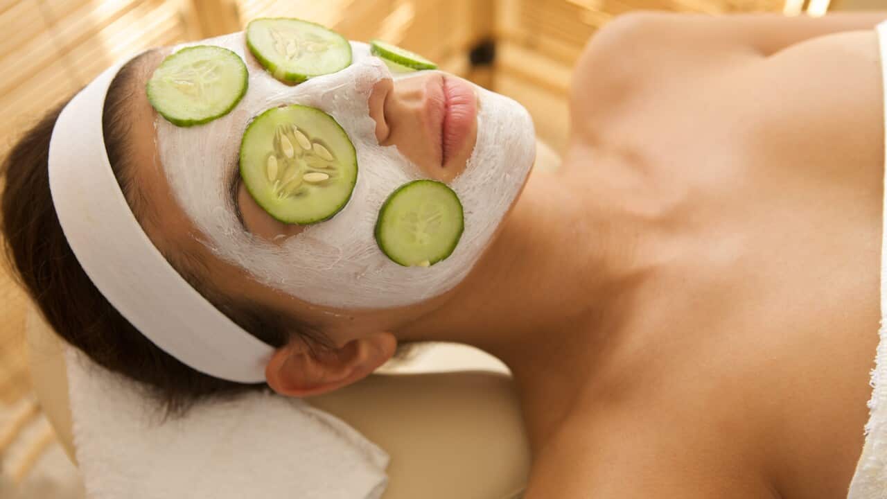 Young woman lying down on massage table with cucumbers on eyes a