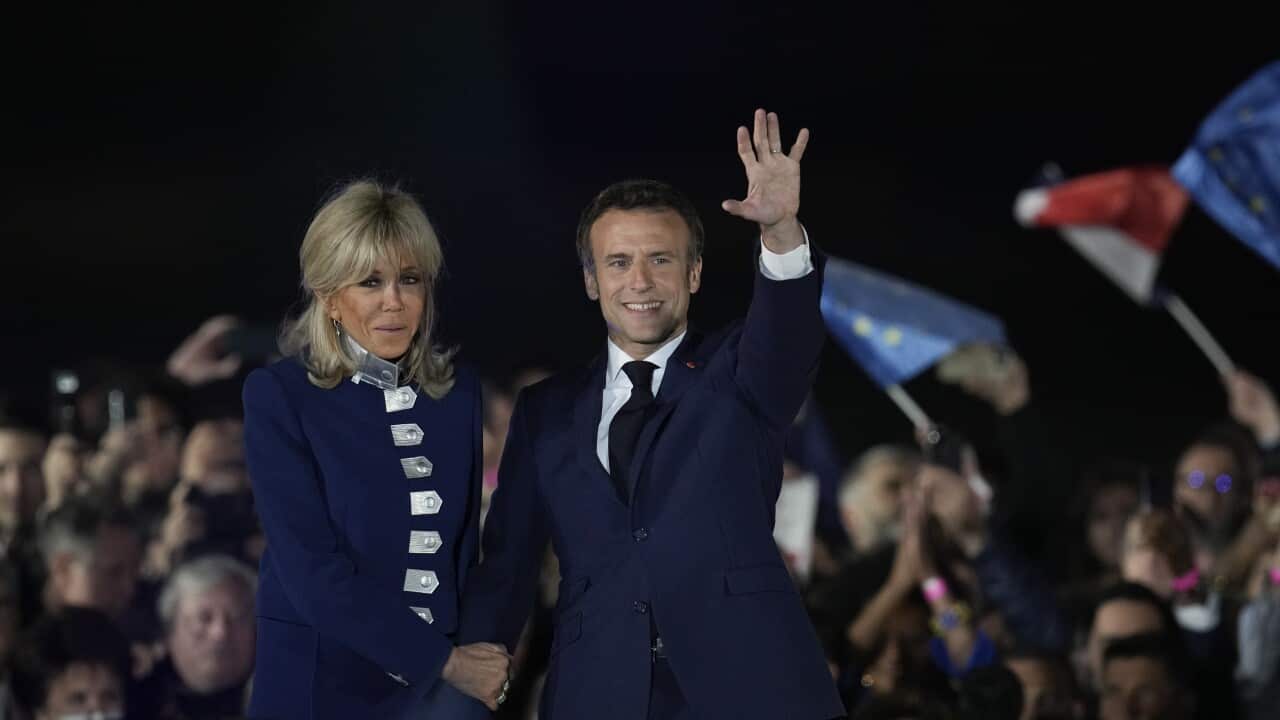 A woman holding a man's arm who is waving to a crowd.