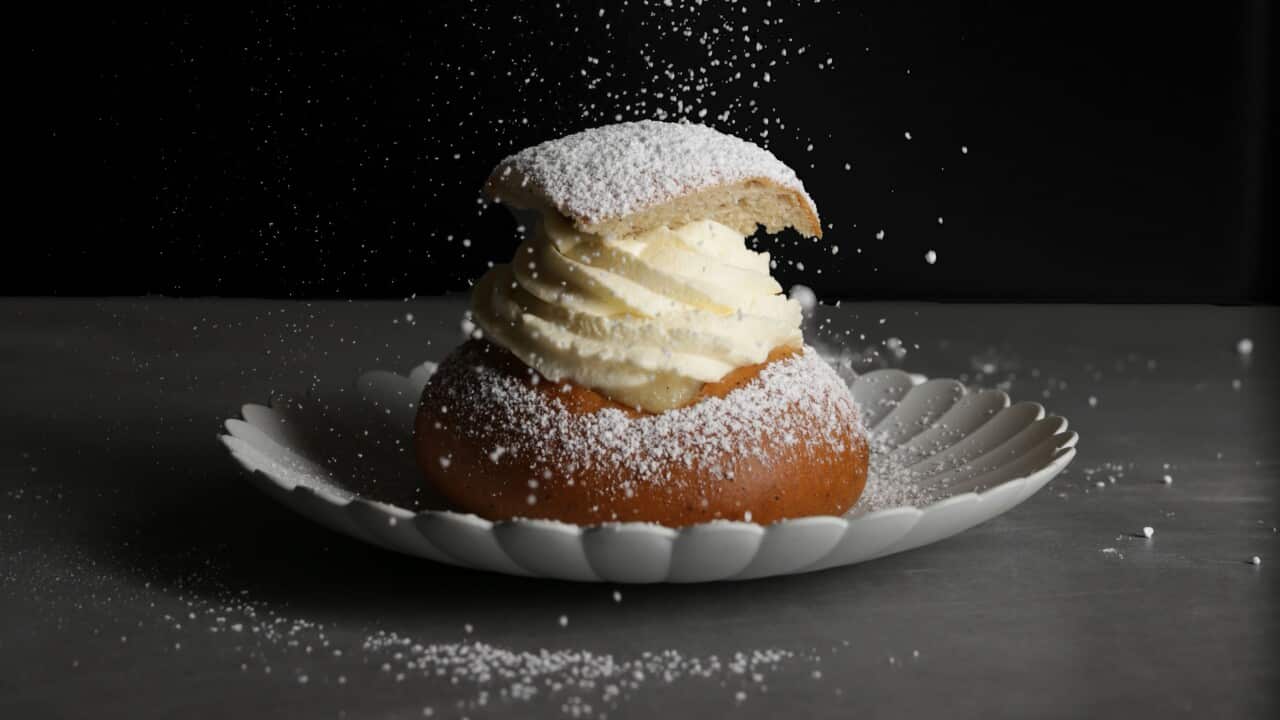 Hand spinrkling icing sugar on to bun topped with whipped cream.