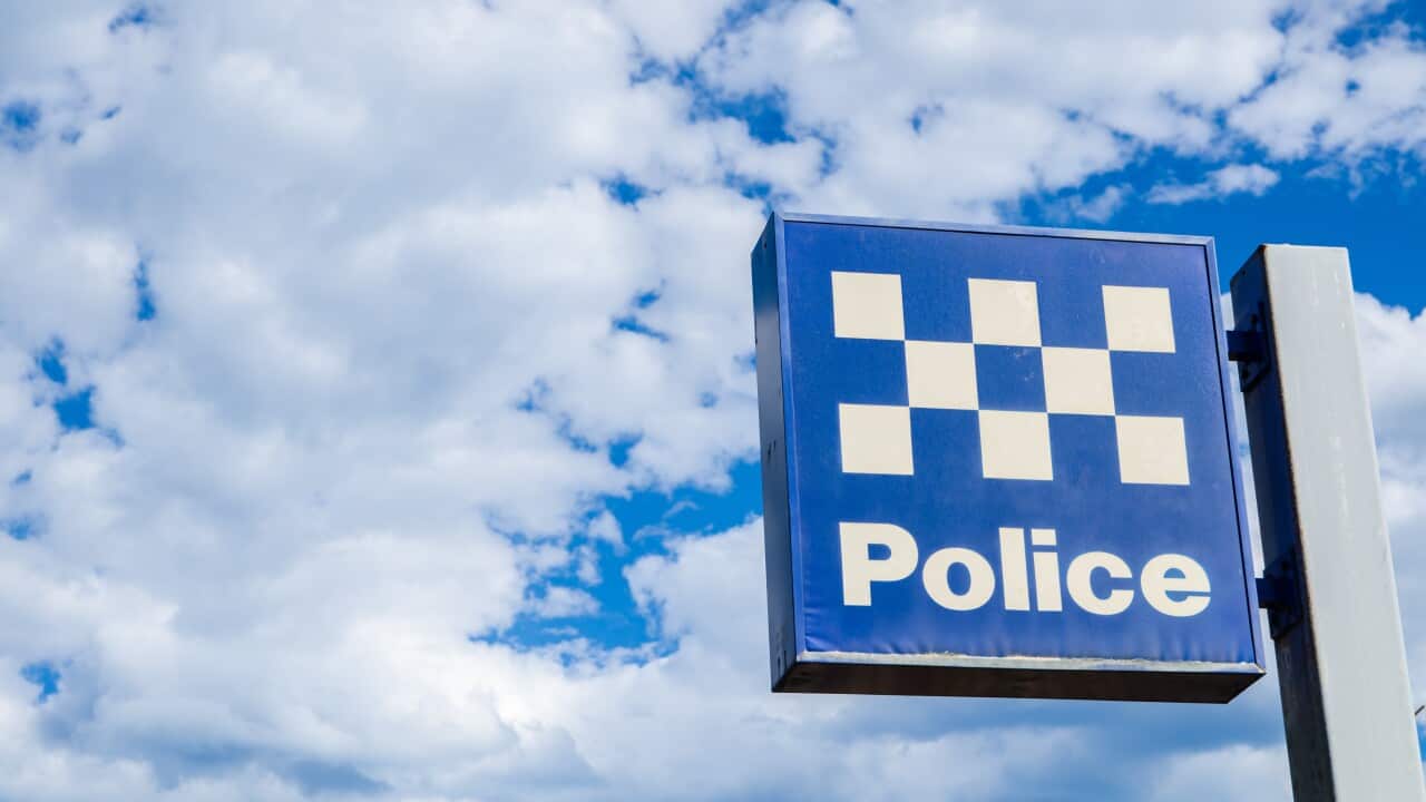A police station sign, against a blue sky with clouds.