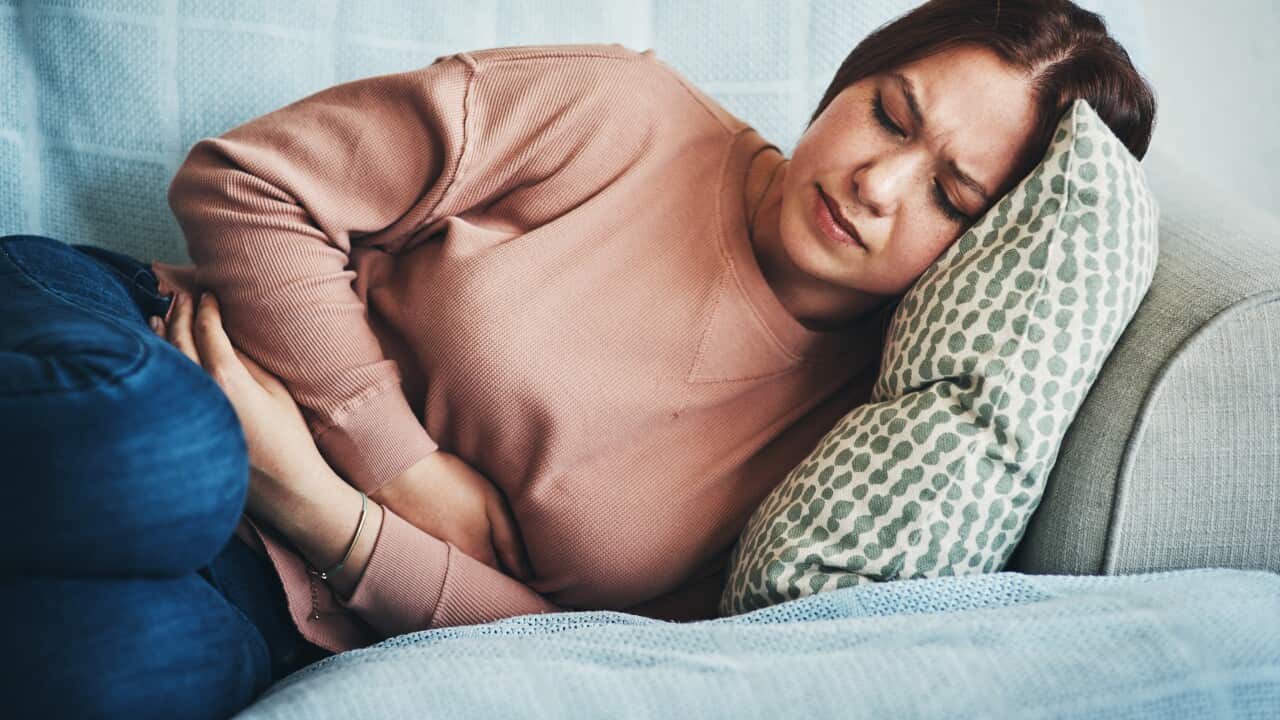 A woman experiencing stomach pain while lying on the sofa at home
