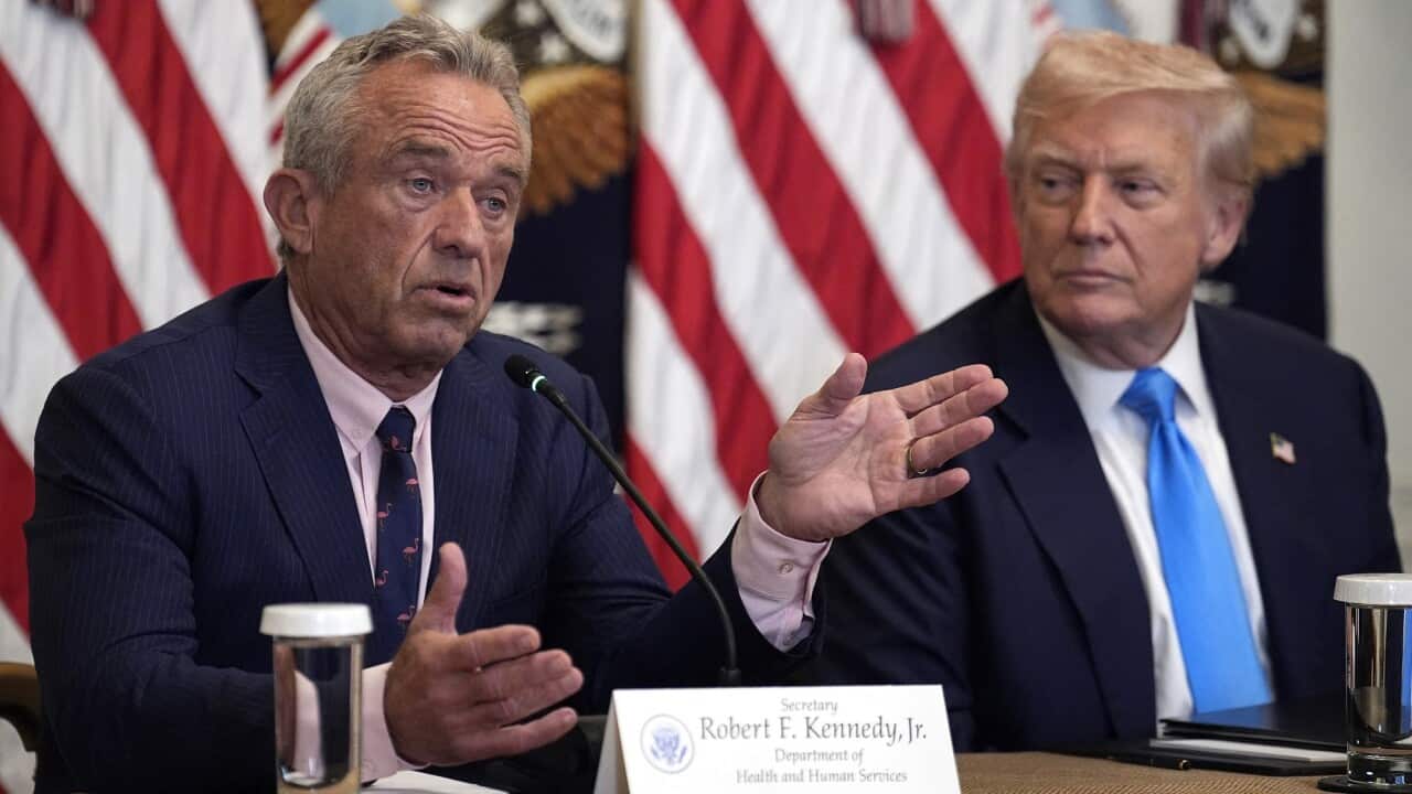 US Health Secretary Robert F Kennedy Junior speaking in front of a microphone. Donald Trump is seated to his left.