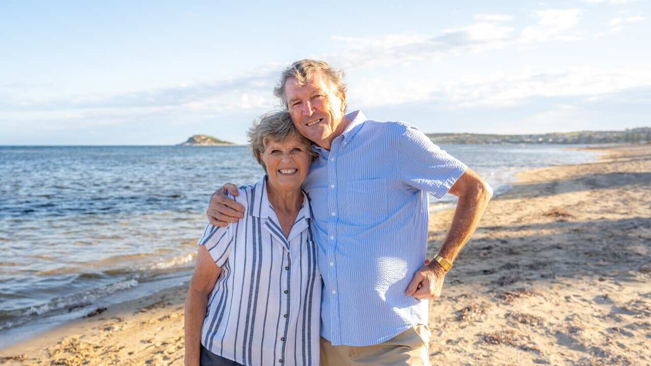 An older couple standing on a beach with their arms around each other.