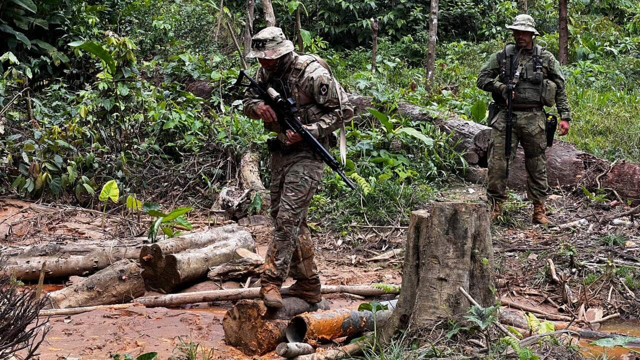 Two officers with guns walking through an illegal mining camp in the Brazilian Amazon.