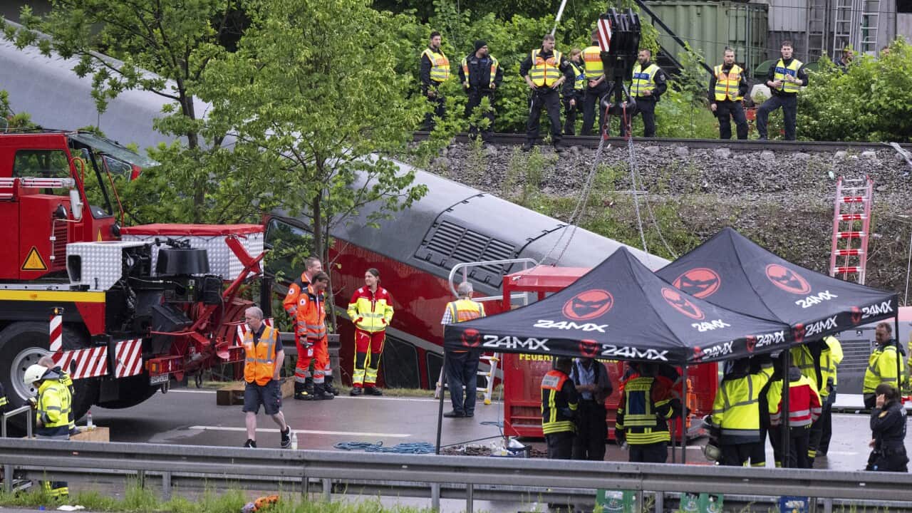 Rescue workers wearing brightly coloured uniforms gather around a train that has derailed.