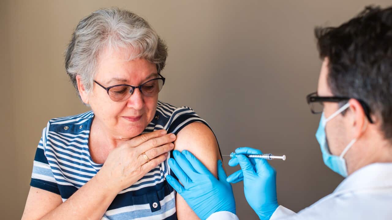 Older woman getting injected with a vaccine by doctor in upper arm.