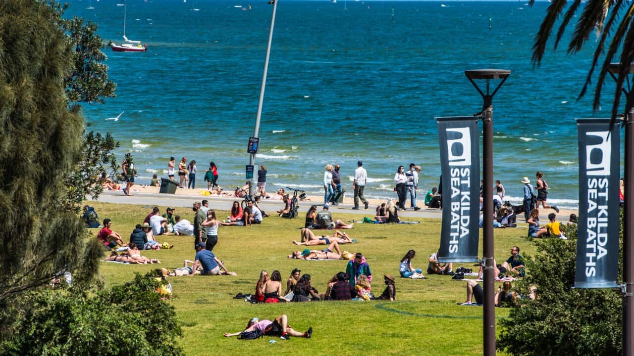 People enjoy conversations and sunbathing on a lawn near Melbourne's popular St Kilda Beach on a warm sunny day.