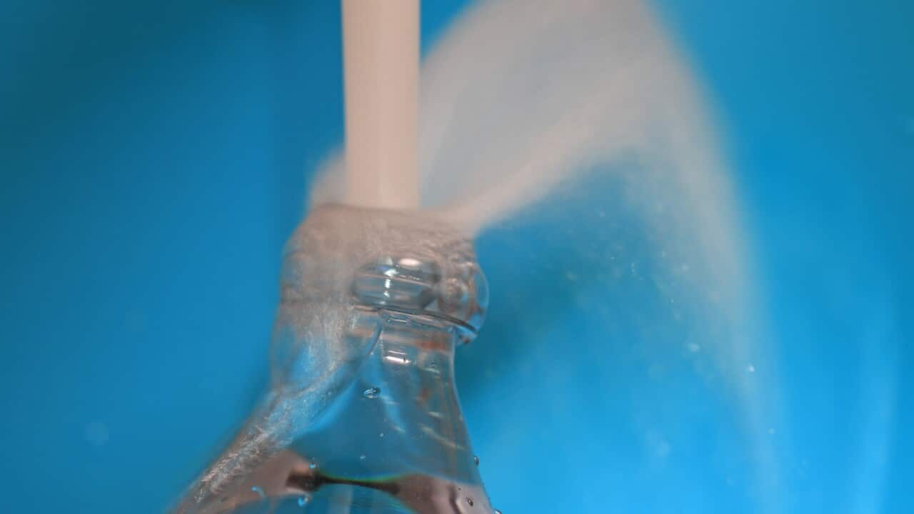 Fresh water from faucet overfilling a plastic bottle against blue background