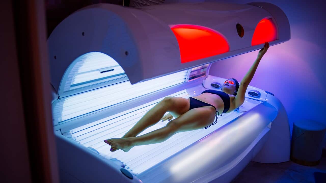A woman in a bikini pulling down the top of a sunbed or solarium