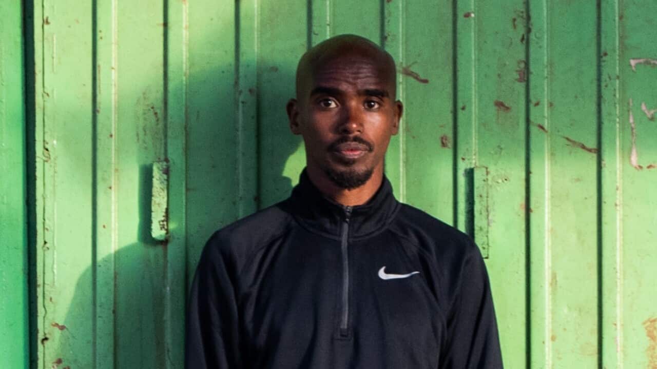 Moh Farah standing against a green shed looking at camera.