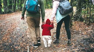 Young active family of hikers walking in the autumn forest with the toddler baby