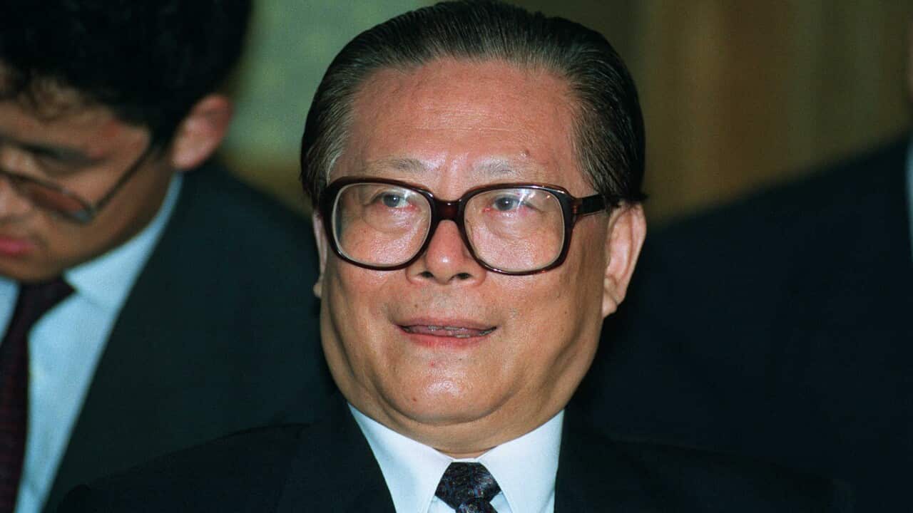 A man wearing a suit and glasses is pictured smiling.