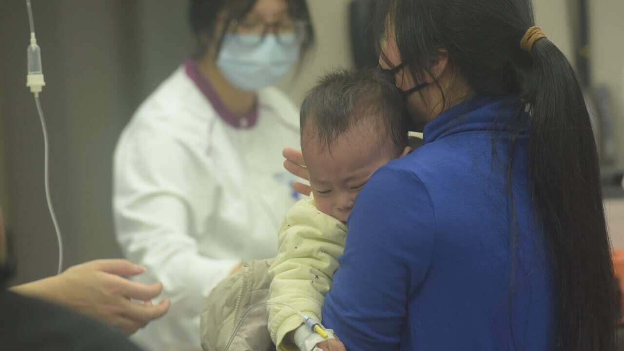A child receiving treatment from doctors at a hospital, held by a woman in a blue top.