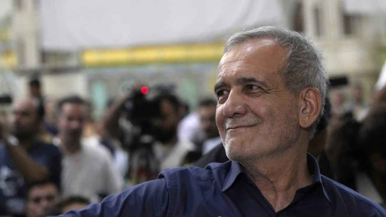 Masoud Pezashkian staring left and smiling. There is a crowd of people behind him.