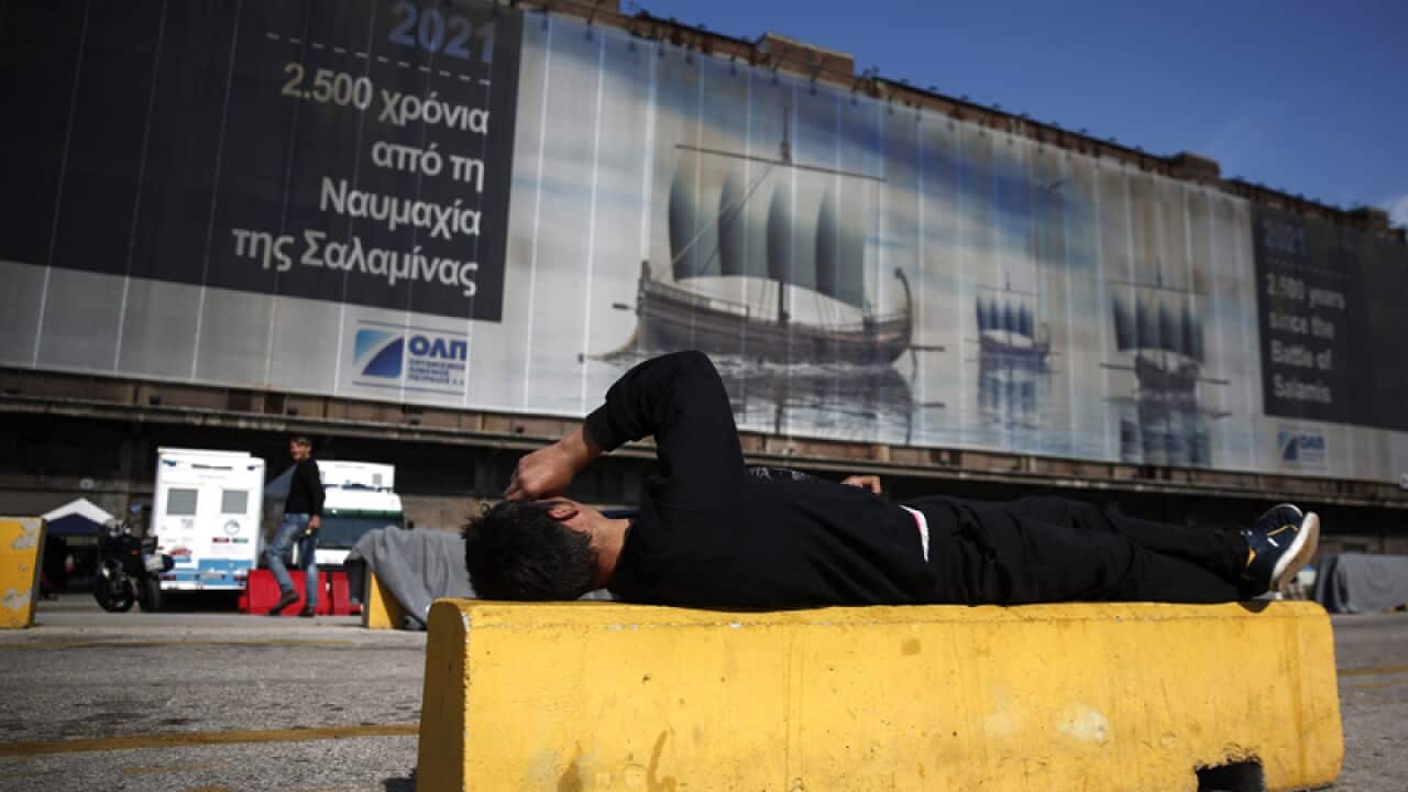 A man rests in front of a giant poster at the port of Piraeus