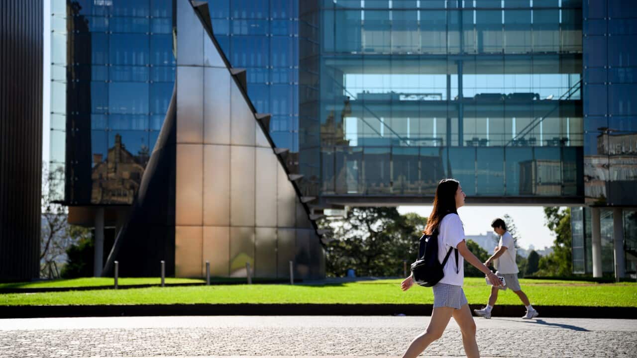 People walking on a footpath, a lawn and a building with a glass facade are in the background.