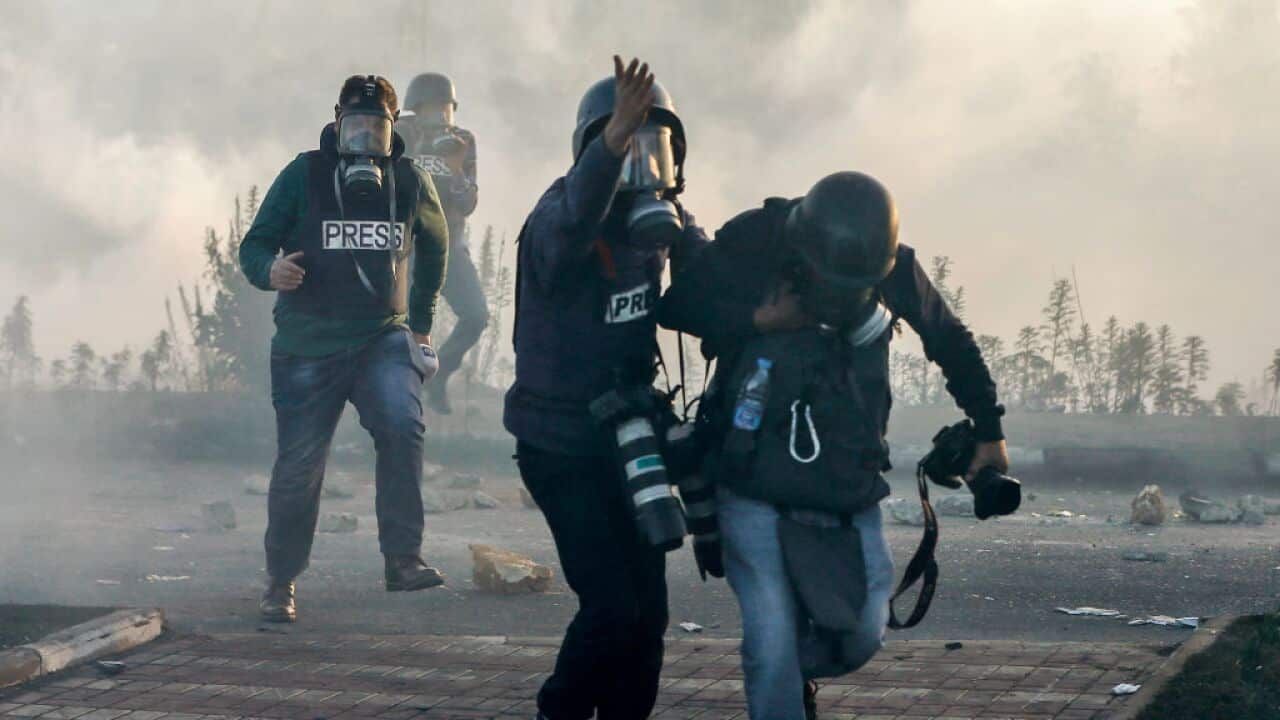 Photojournalists and video journalists wearing gas masks flee from teargas fired by Israeli forces on the West Bank.