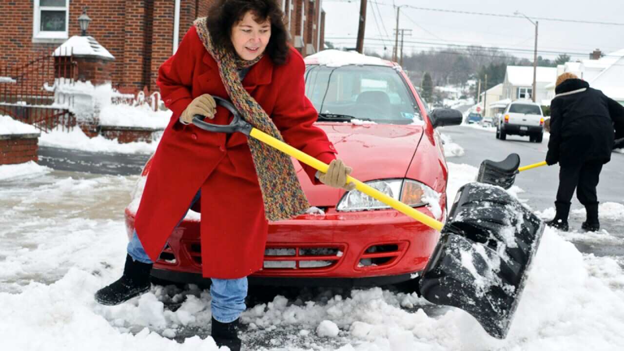 A woman helps shovel out the car of her friend