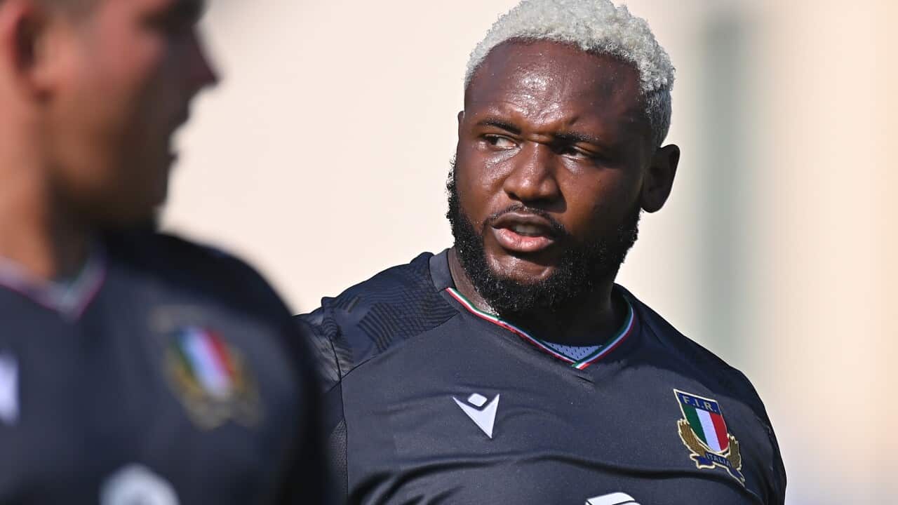 A rugby player walking on a playing field next to his team mate.