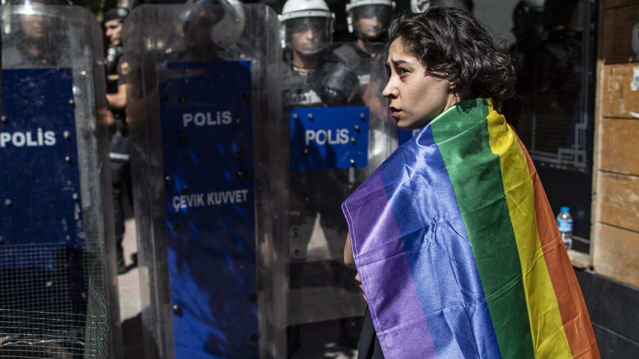 A LGBTQI+ supporter with a rainbow flag standing in front of Turkish police at Istanbul Pride March